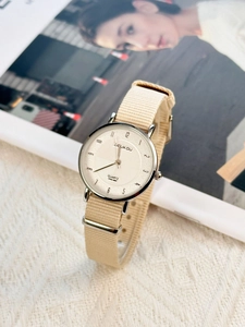 Detail view of a minimalist silver watch with beige nylon strap on a soft knit background