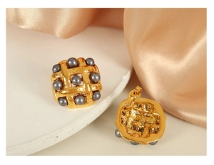 Detailed view of gold woven texture earrings with dark grey pearl inlays on silk fabric