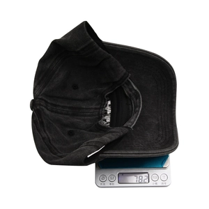 Washable denim baseball cap in dark grey being weighed on an electronic scale
