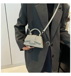 Gros plan du sac à main tissé crème avec détails dorés sur un blazer gris