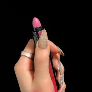 Gros plan d'un rouge à lèvres rose mat dans un étui coloré tenu par des ongles dorés