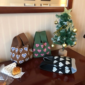 Three knitted tote bags in brown green and black colors with woven heart patterns on wood