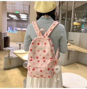 Pink strawberry print backpack with plush charm worn by a model in a cozy cafe setting