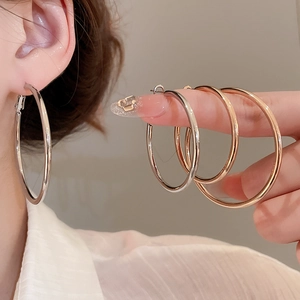Detailed view of large polished silver and rose gold hoop earrings worn on ear
