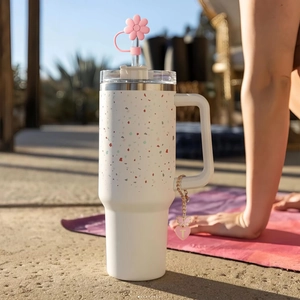 Pink floral straw cover with butterfly charm on a white terrazzo tumbler in outdoor setting