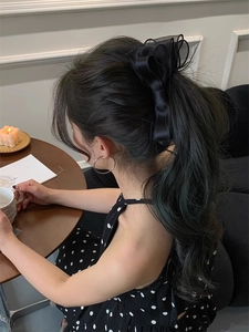 Detail view of a large black double-layered mesh bow hair clip worn on a high ponytail