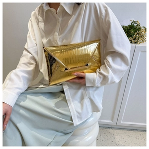 Detail of gold envelope clutch bag with crocodile texture held by a model