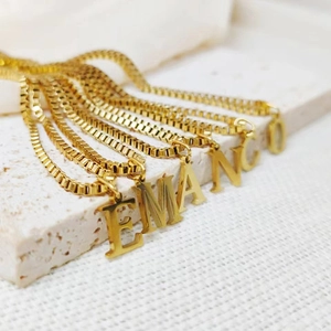 Detailed view of gold stainless steel box chains with capital letter pendants on stone