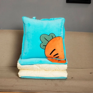 Detail view of a blue plush carrot pattern cushion folding into a travel blanket on a beige sofa