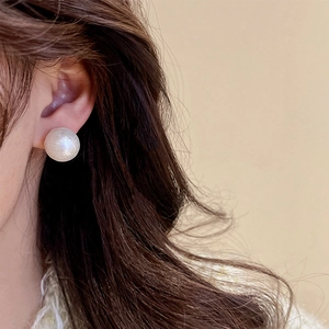 Close-up of a white matte faux pearl stud earring worn on a model's ear lobe