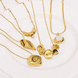 Five assorted 18K gold-plated titanium steel necklaces set on a white ceramic tray