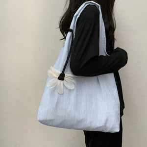 Close-up of light blue pleated shoulder bag with a white flower charm accessory