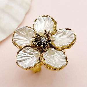 Macro detail of a golden flower ring featuring white shell petals and a pearl center