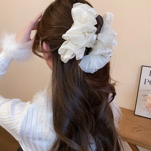 Detail of a large white ruffled hair claw with sparkling rhinestones on wavy hair