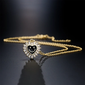 Gold sunflower smile necklace with black heart and zircon stones on a dark reflective surface