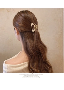 Detail view of a gold hollow D-letter metal hair claw clip worn on a woman's hair