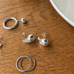 Close-up of minimalist 925 sterling silver whale earrings and rings on a wooden surface