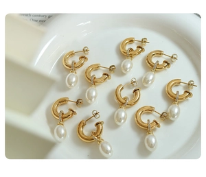 Macro detail of gold C-shaped earrings with drop pearls and crystal accents on a dish