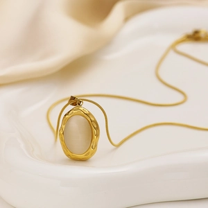 Elegant gold titanium steel necklace with vintage cat eye opal pendant on a ceramic tray