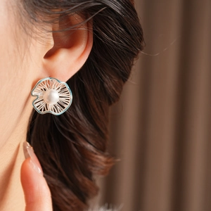 Detailed view of silver flower earrings with white pearl center on model ear