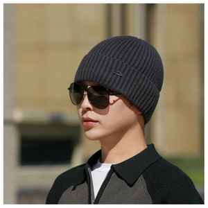 Detailed close-up of dark grey ribbed knit beanie with small metallic mountain buckle