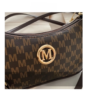 Close-up of golden M logo and monogram printed leather detail on brown handbag