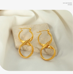 Macro detail of gold-tone infinity twist earrings displayed on a natural textured stone