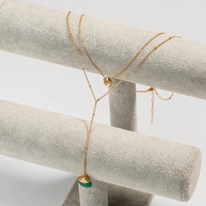 Détail d'un collier doré multicouche avec pendentif en pierre verte et charme organique