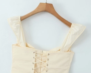 Close-up of the back cross-lace-up design and pleated straps on the yellow mini dress