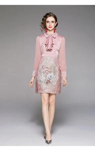 Detail of pink satin dress featuring floral embroidery, sheer sleeves and ruffle collar