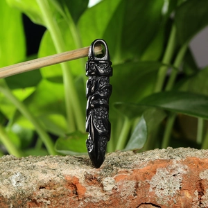 Close-up of black stainless steel dagger pendant with intricate textures on red brick