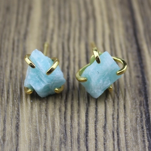 Macro detail of raw light blue stone stud earrings with a four-prong gold metal setting