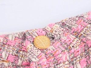 Détail de la texture du tweed rose avec un bouton rond doré décoratif en relief