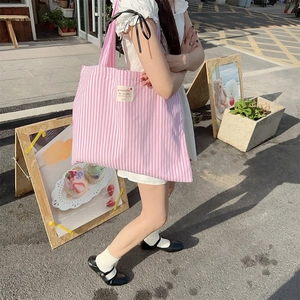 Pink and white striped canvas tote bag with a woven label shown in a street scene