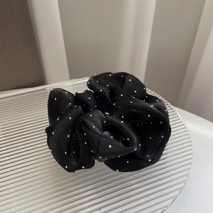 Macro detail of a black satin scrunchie with silver accents on a ribbed glass tray