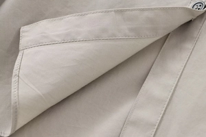 Detailaufnahme des khakifarbenen Baumwollhemdes mit feinen Nähten und Harzknopf