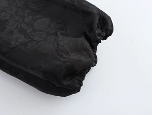Detail aus schwarzem Jacquard-Stoff mit Blumenmustern und elastischen Raffbündchen