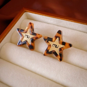 Close-up of tortoise shell resin star earrings with gold miu logo on velvet background
