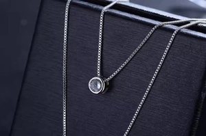 Close-up of a silver box chain necklace with a round bezel-set zircon on leather