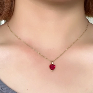 Detail of a heart-shaped red gemstone necklace with a minimalist gold chain on a model