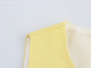 Dettaglio della spallina di un vestito giallo senza maniche con trama a pieghe e fodera bianca