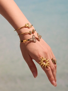 Close-up of golden butterfly bracelets and sun rings worn on hand by a blue pool