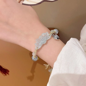 Close-up of hand-woven bracelet featuring a blue-green lotus charm and light yellow cord