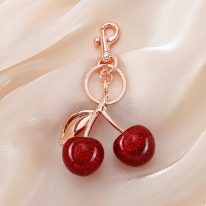 Detailed view of red glitter resin cherry keychain with rose gold hardware on beige silk