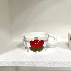 Detail of hand-painted red smiley flower and purple plaid on a ceramic coffee mug