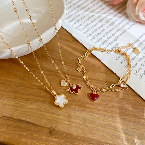 Detail view of gold-plated jewelry set with red heart and white clover charms