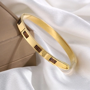 Detail of gold titanium bangle with amber square zircons on brown leather box and silk