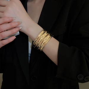 Detailed close-up of a high-polish gold cuff bracelet with rippled texture on a model