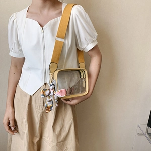Detail of transparent PVC crossbody bag with yellow strap and printed silk scarf accessory