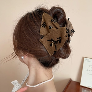 Detail of vintage brown bow hair claw with black pattern and gold charm on model's hair